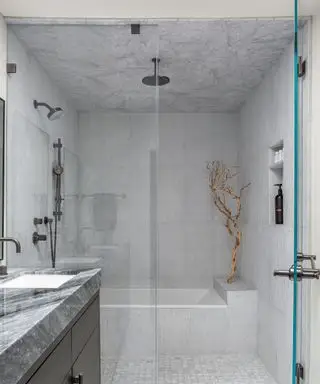 Banheiro com box amplo com azulejos de mármore e tela de vidro, armário de banheiro preto com bancada de mármore cinza