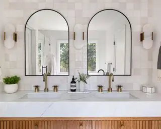 Doppio lavabo in marmo con parete con texture di piastrelle quadrate e due specchi ad arco.webp