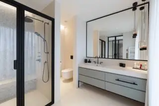 cuarto de baño moderno y neutro con accesorios y accesorios negros, suelo de piedra color crema, ducha con pared de mosaico y banco de ducha, puertas de ducha negras