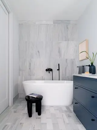 baño con azulejos grises, bañera blanca, ducha de mano y tocador azul marino