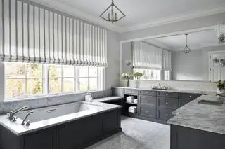 Baño blanco con muebles grises y persiana a rayas grises y blancas.