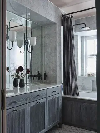 Baño alicatado con azulejos de mármol y equipado con un tocador de madera gris.