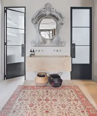 Master en suite con tappeto orientale con motivi floreali su pavimento in legno, specchio ovale francese del XIX secolo con cornice grigia decorata sopra grande vasca in pietra incorniciata da ante Crittal.