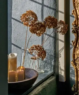 Primo piano della ciotola con candele e fiori secchi in vaso di vetro sul davanzale della finestra.