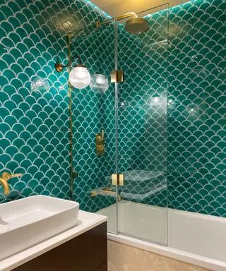 Moderní koupelna se zelenými vroubkovanými obklady, mosaznými svítidly a armaturami, elegantní nástěnné svítidlo s mosazným svítidlem a skleněným difuzorem, páskové stropní osvětlení nad sprchou