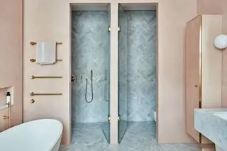 Un bagno rosa con vasca bianca e cabina doccia con hardware dorato