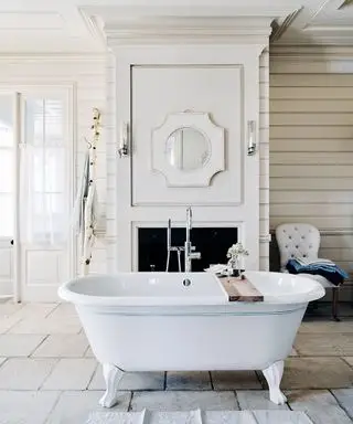 Un bagno bianco con una vasca autoportante bianca con un dettaglio di linea blu davanti a un caminetto