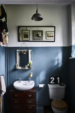 Et hvidt og blåt badeværelse i en tidstypisk ejendom med hvid håndvask og 21 skilt over toilettet