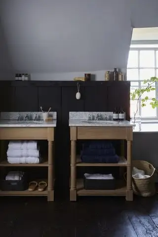 baño tipo loft con paneles de madera oscura, pisos negros, dos tocadores independientes con estantes abiertos y encimeras de mármol