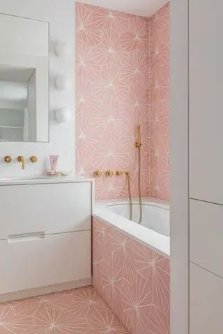 baño blanco con pisos y paredes con motivos rosas, accesorios y accesorios dorados, cómoda blanca, azulejos blancos, espejo, luces de globo