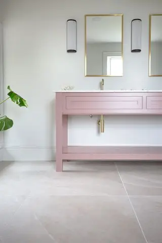 baño neutro con tocador rosa, baldosas, espejos dorados y apliques