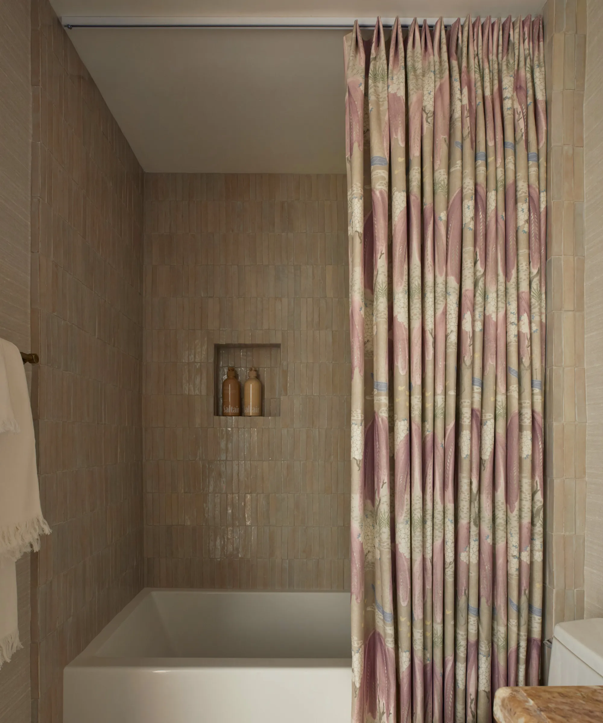 ein Badezimmer mit zartrosa gefliesten Wänden, einer weißen Einbauwanne und einem rosafarbenen Duschvorhang an der Decke' loading='lazy' title=