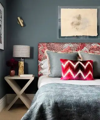 Um quarto com uma parede azul atrás de uma cama com cabeceira estampada em vermelho, branco e azul e almofadas e roupas de cama complementares