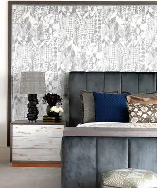 Uma cama de veludo cinza com um mural de parede estampado branco e cinza atrás