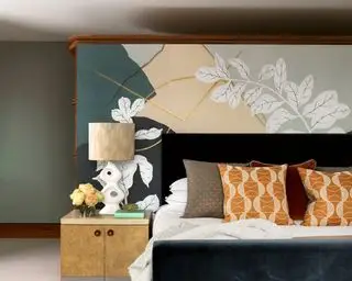 Uma cama preta com almofadas estampadas em laranja e um mural floral atrás