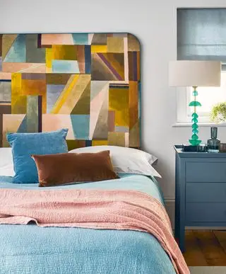 Uma cabeceira grande com um padrão colorido e abstrato em uma cama com roupa de cama azul