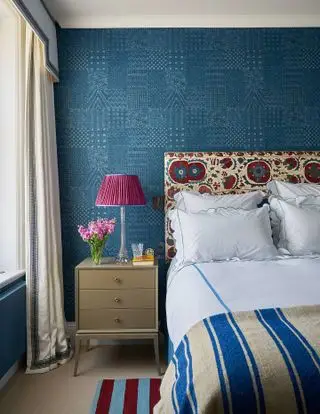 chambre bleue avec papier peint bleu, tête de lit en tissu à motifs, jeté et literie à rayures bleues, chevet, lampe rose