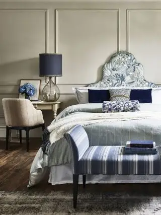 chambre bleue et blanche avec murs taupe, literie bleue et blanche, repose-pieds, parquet, lampe bleue, fauteuil, table d'appoint
