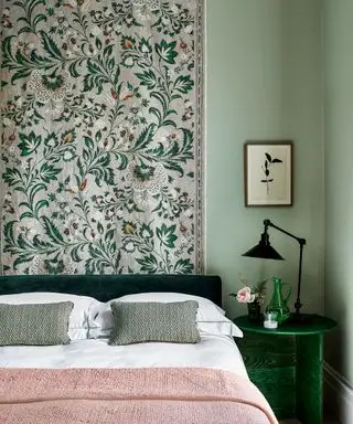Ein Bett mit einer rosa Decke vor einem grün-rosa Blumenwandbehang