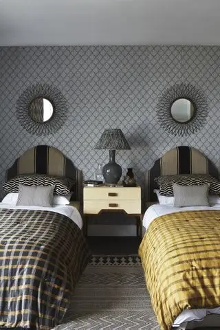 Lits jumeaux simples dans la chambre, tête de lit noire et grise, couettes à carreaux dorés et noirs