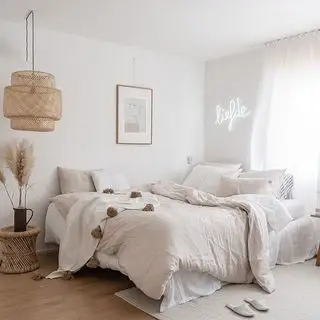 chambre avec lit habillé de draps en lin et suspension en rotin et enseigne au néon blanc