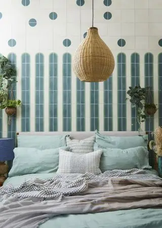 chambre avec mur carrelé bleu et gris derrière le lit, un abat-jour en rotin est suspendu au centre de l'image