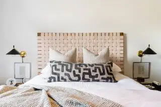 chambre neutre avec tête de lit texturée, coussins à motifs et deux appliques murales noires