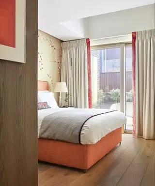 Ein Beispiel für Ideen für Schlafzimmervorhänge: taupefarbene Vorhänge mit orangefarbenem Samtfutter in einem Schlafzimmer mit orangefarbenem Bett und Holzboden