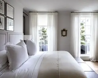 Ein Beispiel für Ideen für Schlafzimmervorhänge, das ein Schlafzimmer mit weißen Wänden, Laken und Vorhängen auf einer schwarzen Schiene zeigt