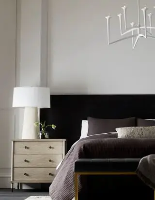 Artteriors の黒いヘッドボードと木製のチェストを備えた白いベッドルーム