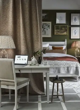 Schlafzimmer-Heimbüro, grüne Wände, Vorhang, weißer Schreibtisch und Stuhl, weiß gestrichenes Bett, Galeriewand, Teppiche, Tischlampe auf Glasbasis