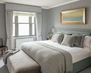 Graues Schlafzimmer mit einem stilvollen Bett und Ottomane, das luxuriöse Schlafzimmerideen zeigt.