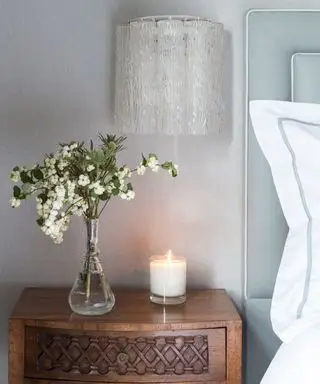 Luxuriöse Schlafzimmerideen, illustriert durch eine Kerze und eine Blumenvase auf einem Nachttisch aus dunklem Holz.