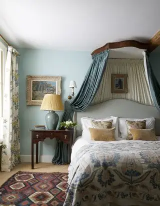 Blaues Schlafzimmer mit weißer Decke, Bettwäsche, blauem Stoffhimmel, Blumenvorhängen, Nachttisch, taupefarbenen und geblümten Kissen, Teppich auf dem Boden