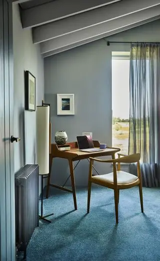 domáca kancelária so sivými stenami, modrý koberec, moderný stôl a stolička z polovice storočia, stojaca lampa, umelecké dielo