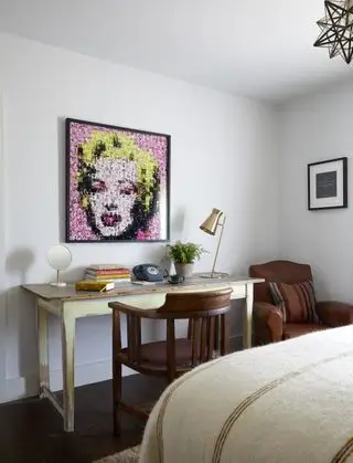 hosťovská kancelária s rustikálnym stolom a mahagónovým kreslom, kožené kreslo v rohu, posteľ v popredí, potlač Marilyn Monroe, mosadzné stolové svetlo