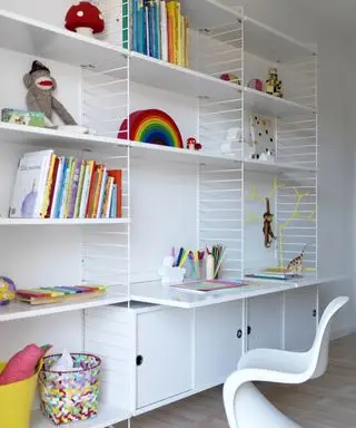 Decoración de habitación para niños con paredes blancas, escritorio y estantería abierta con libros y juguetes coloridos.