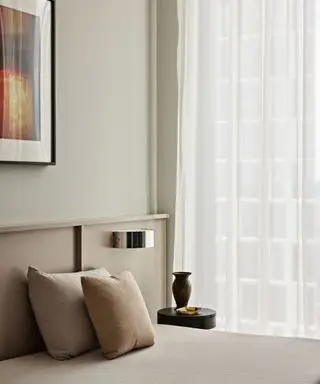 Un dormitorio neutro, con luz natural y cortinas blancas transparentes.