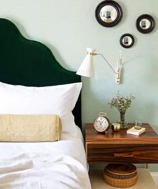Un dormitorio empapelado en verde con una cabecera de terciopelo verde y una lámpara de noche montada en la pared