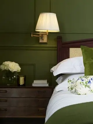 dormitorio verde con lámpara de pared con brazo giratorio, muebles de caoba, manta verde, cojín, cojín floral, ropa de cama blanca