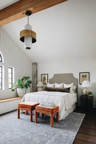Schlafzimmer mit Bett und Fußhockern, Nachttischen, gewölbter Decke mit Anhänger, weißen Wänden und Holzboden mit Teppich