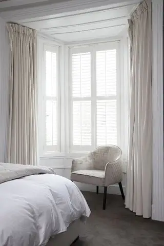 Weißes Schlafzimmer mit Vorhängen und Fensterläden