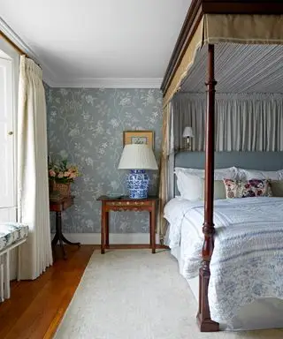 Schlafzimmer mit blau gemusterter Tapete und Himmelbett aus Holz