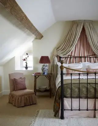 Schlafzimmer im Dachgeschoss mit Baldachin, Eisenbett, Kokosteppich, gepolstertem Stuhl, Beistelltisch, Teppich, Balken, Rosatönen