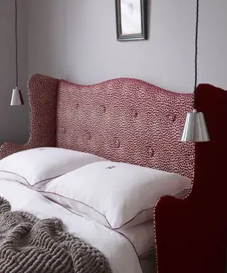 Detailní záběr postele s vyraženým červeným a bílým čelem s bílým povlečením a dvěma závěsnými lampami