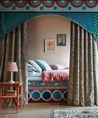 Ein doppeltes Himmelbett mit farbenfroher Bettwäsche und schweren Vorhängen und Querbehang. Schichten aus Material, Farbe und Muster, um ein gemütliches Eckbett zu schaffen