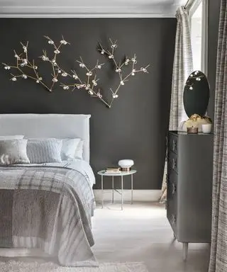 Eine graue Schlafzimmeridee mit dunkelgrauen Wänden, einer von der Natur inspirierten Lichtinstallation und grauen Holzböden