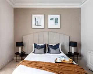 Eine graue Schlafzimmeridee mit warmen braungrauen Wänden, taupefarbenem Kopfteil und einem ockerfarbenen Überwurf auf dem Bett