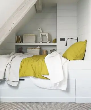 Un esempio di idee per la camera degli ospiti che mostra un letto bianco incorporato in un'alcova accanto a uno scaffale
