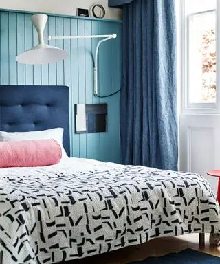 Un esempio di idee per la camera degli ospiti che mostra una parete rivestita di pannelli blu dietro un letto con una testiera blu navy e un copriletto monocromatico